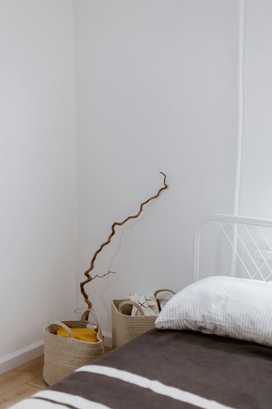 A simple and clean bedroom corner with woven baskets and a decorative branch against a white wall.
