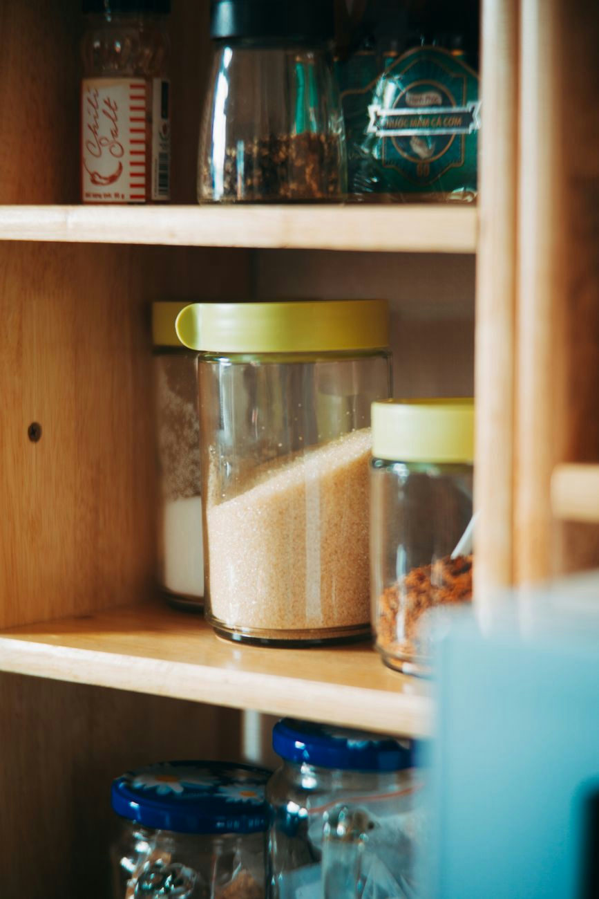 Neatly arranged kitchen pantry with glass jars and ingredients on wooden shelves.