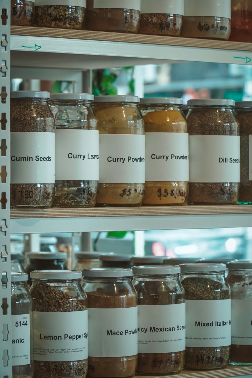 Close-up shot of various spices in labeled glass jars on wooden shelves in a store.