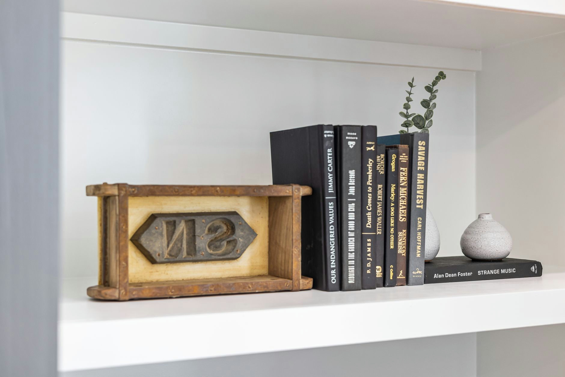 Minimalist bookshelf with black hardcover books, small vases, and decorative cube for elegant decor.