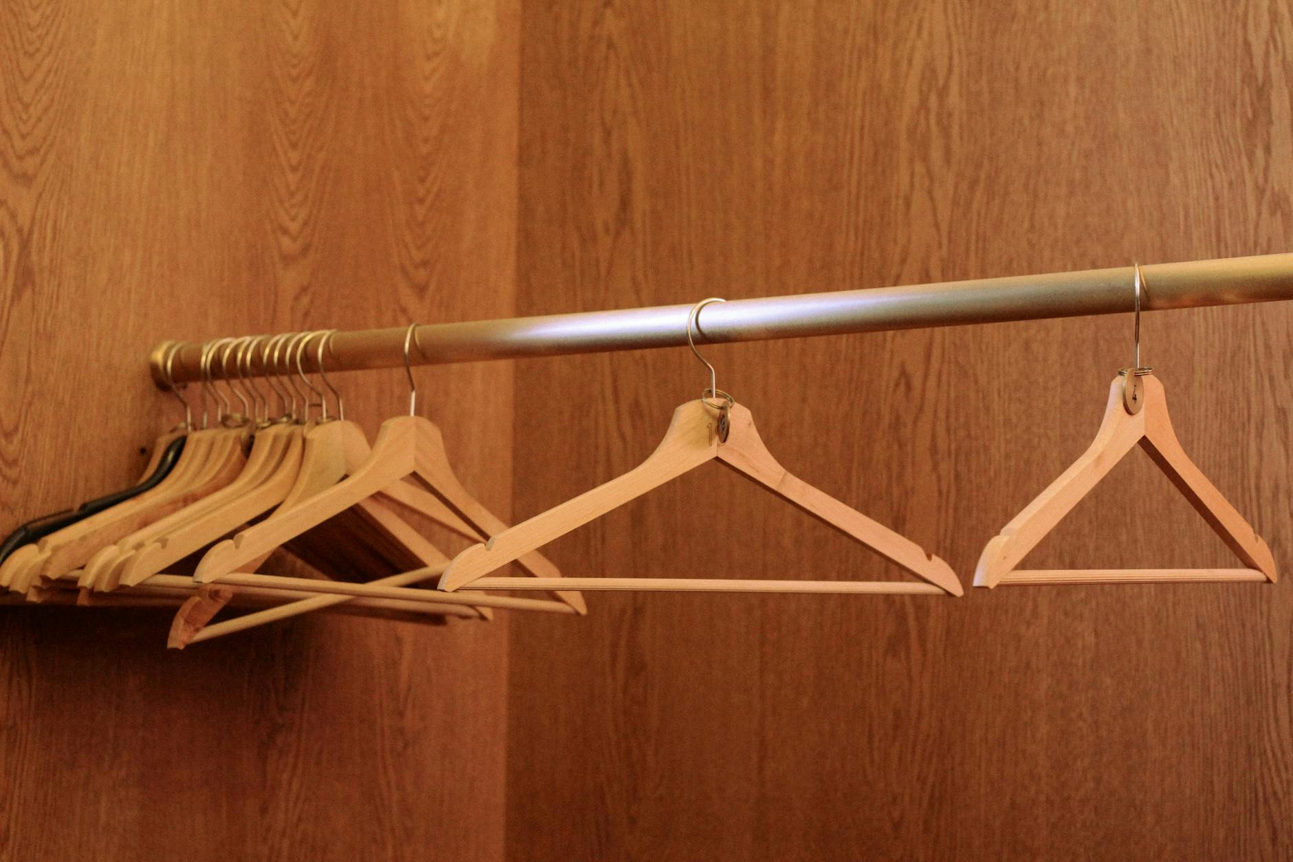 A row of wooden hangers on a metal rod in an empty, wood-paneled closet.