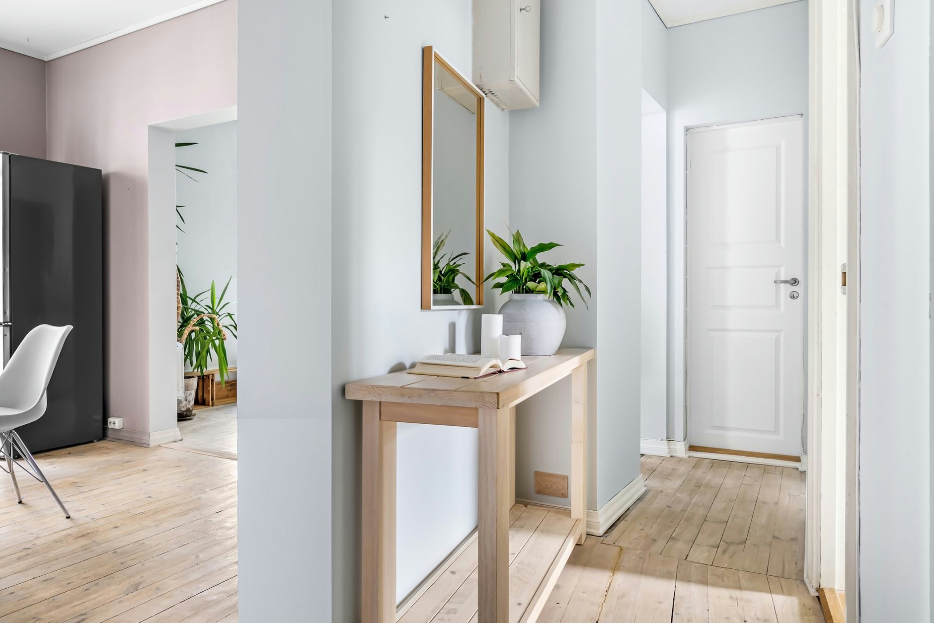 Bright hallway interior featuring minimalist decor, a mirror, and lush plants for a serene ambiance.