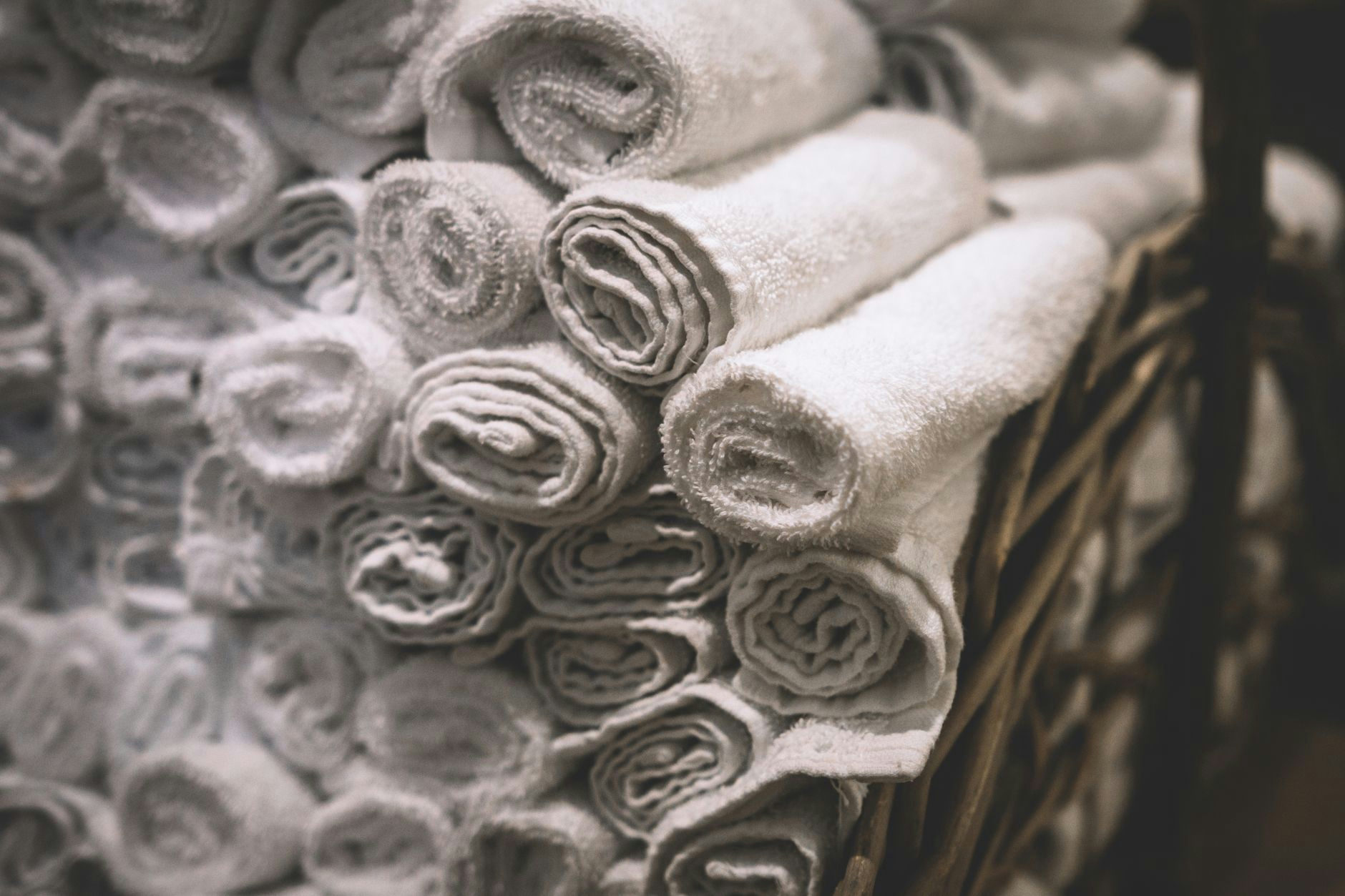 Stack of neatly rolled white towels in a woven basket, perfect for spa or bathroom settings.