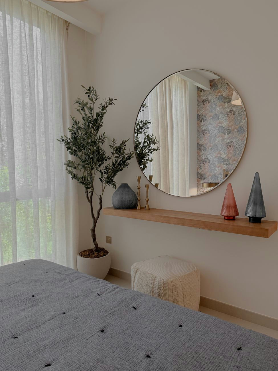 Elegant minimalist bedroom with round mirror, plants, and stylish decor elements.