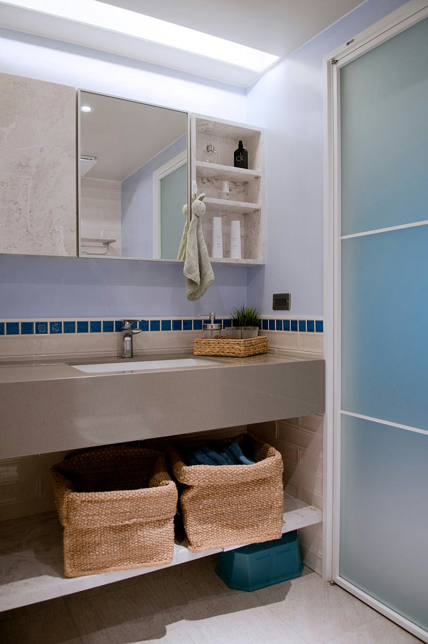 Small mirror and toiletries on shelf above sink under rectangular lamp in bright contemporary bathroom
