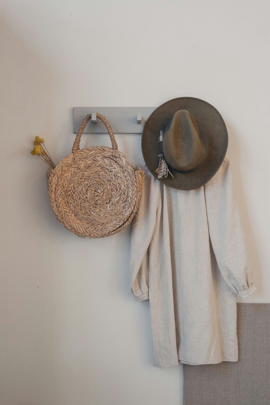 A hanging straw bag and hat with a beige dress on a white background.