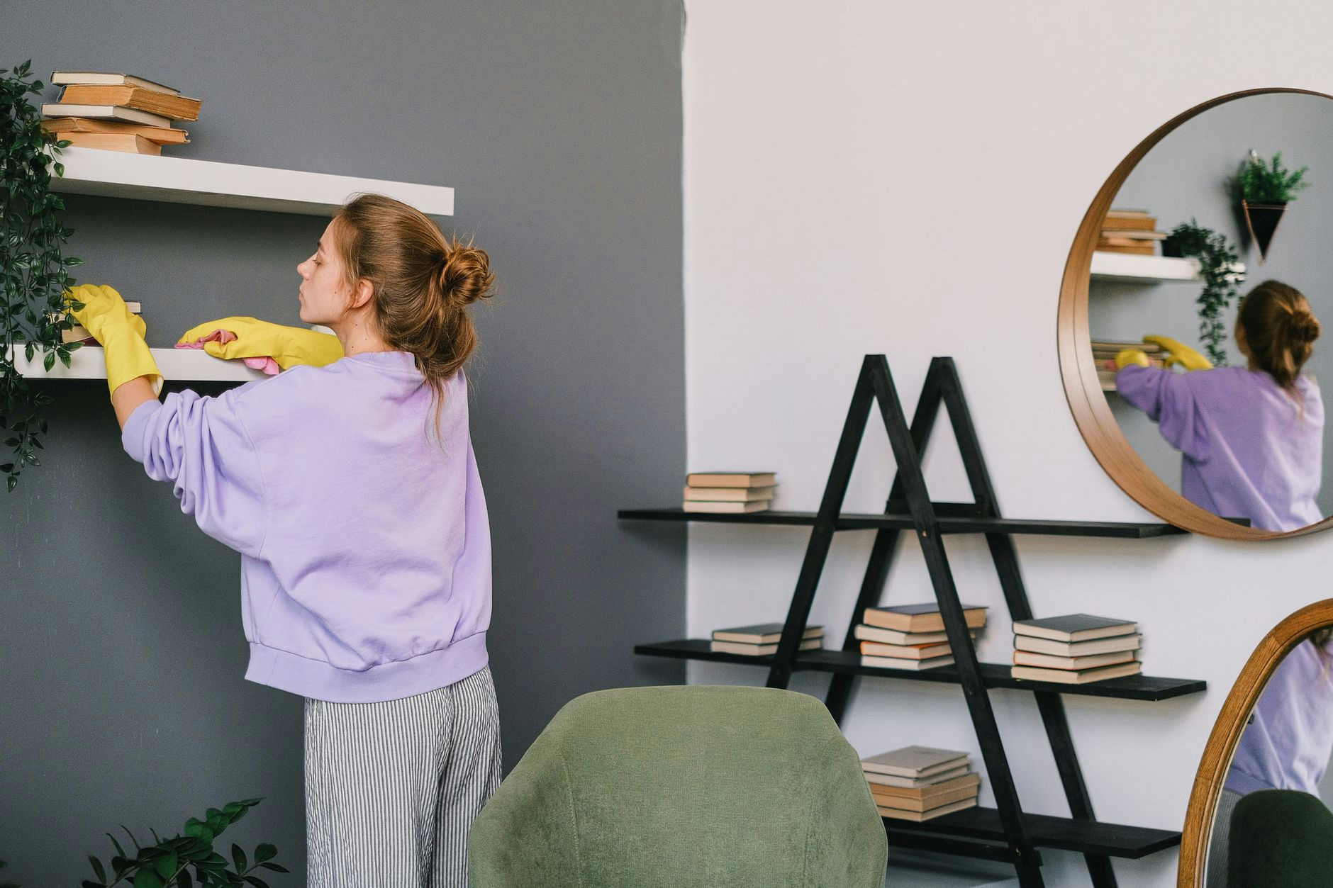 A woman cleans shelves in a stylish living room with mirrors and decor.