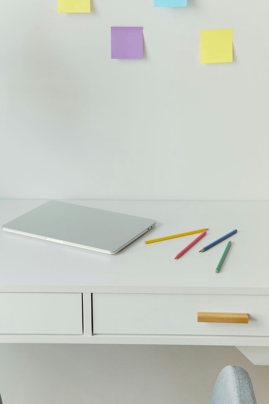 A minimalist home office desk with a laptop and colored pencils on a white surface.