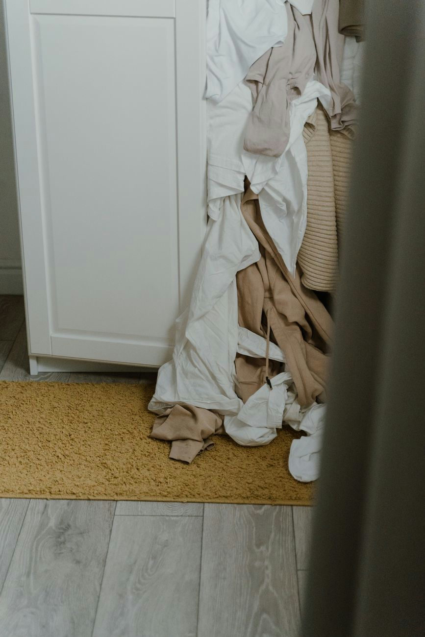 A cluttered wardrobe with clothes spilling onto the floor, reflecting fast fashion impact.