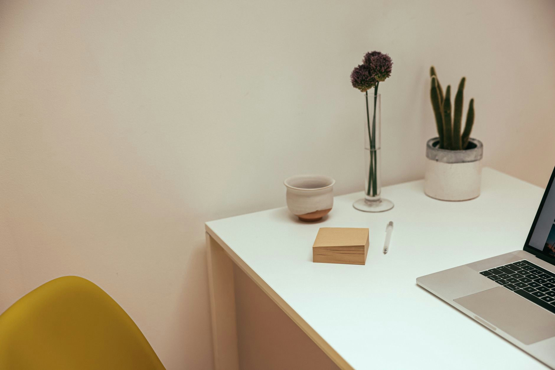 A clean and modern minimalist desk setup with a laptop, plants, and a ceramic cup.