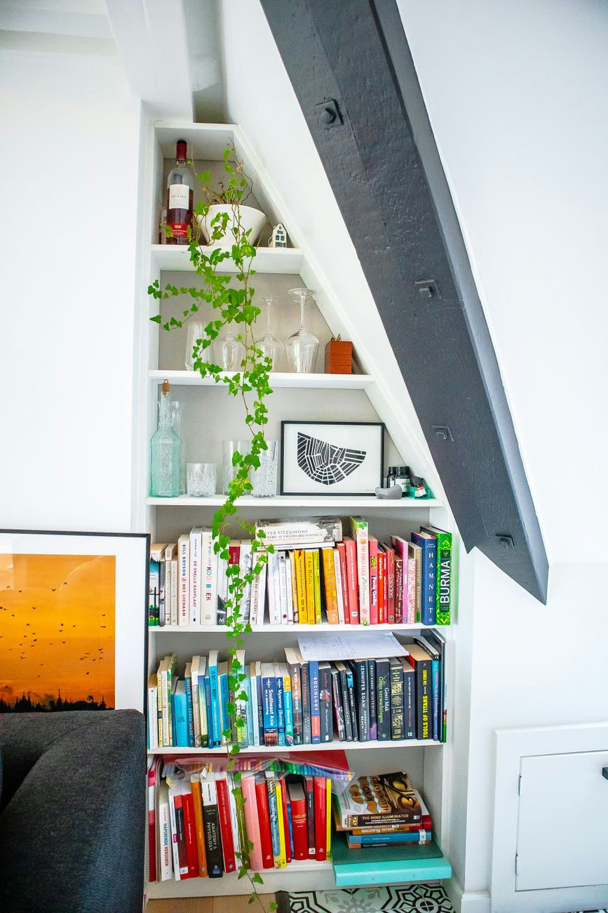 A stylish bookshelf with plants and books in a modern room under stairs.