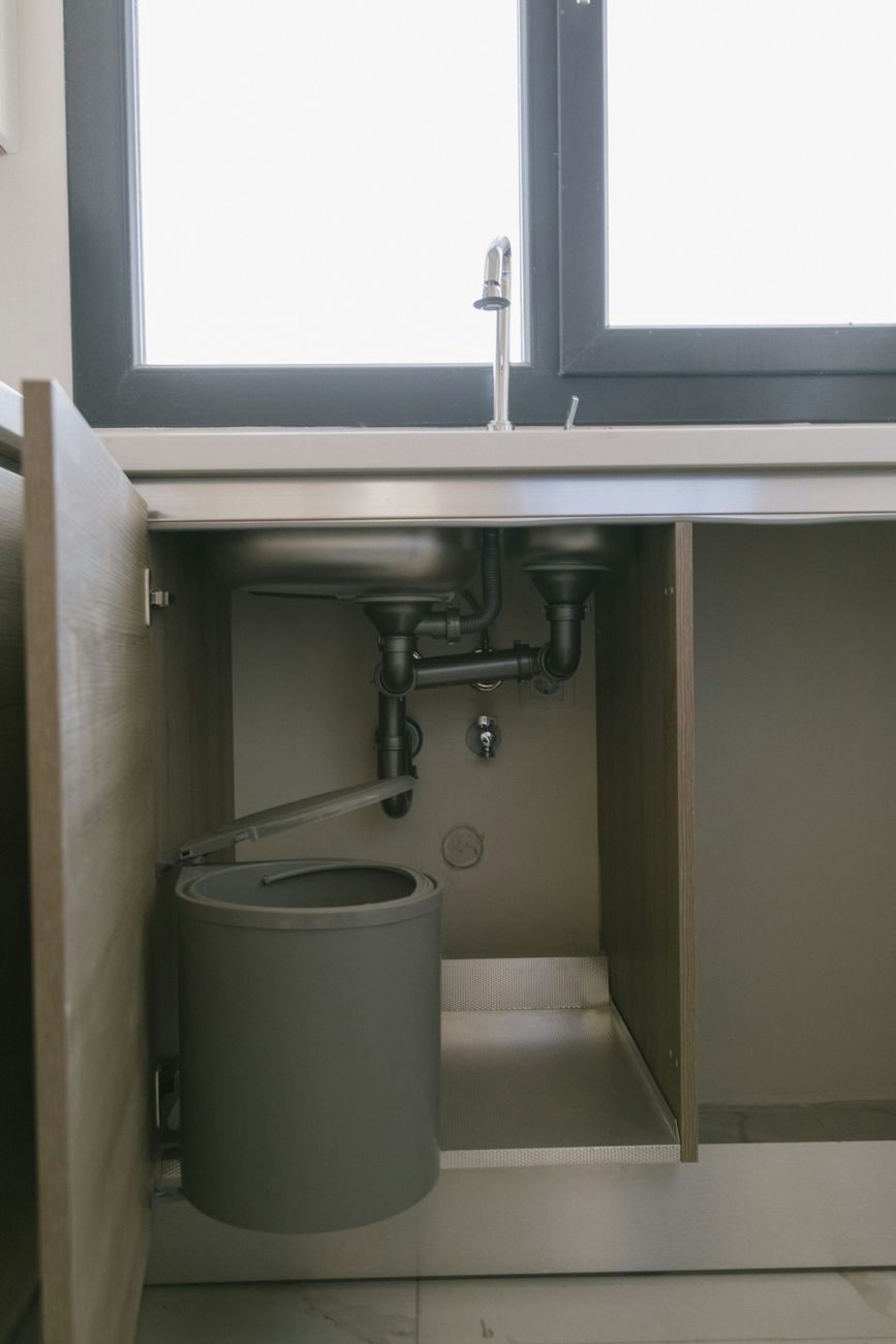 Under-sink view of modern plumbing with garbage bin in an Istanbul apartment kitchen.