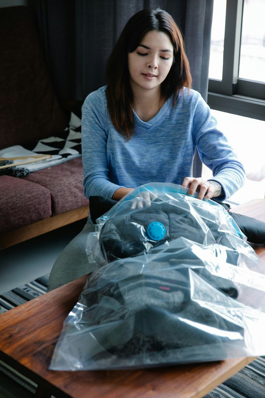 Young woman using vacuum seal bags to pack clothes indoors.