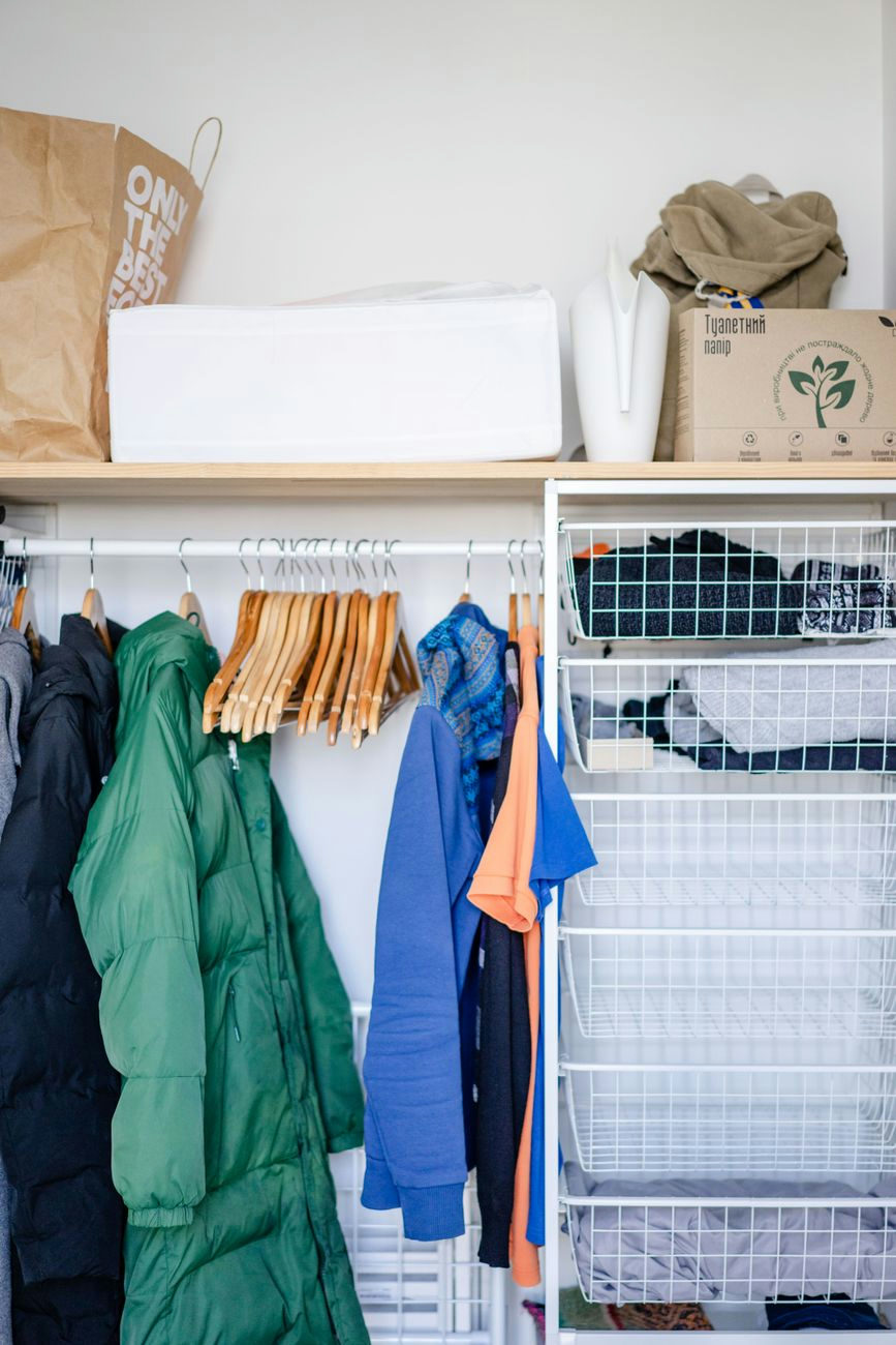 Neatly arranged clothes on hangers in a closet with wire storage baskets offering home organization